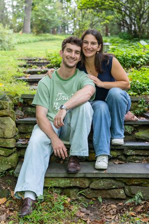 Happy young couple sitting together on stone steps in a lush green garden, smiling warmly at the camera.