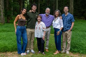 Six people smiling together outdoors in a lush green forest setting for a family portrait photo.