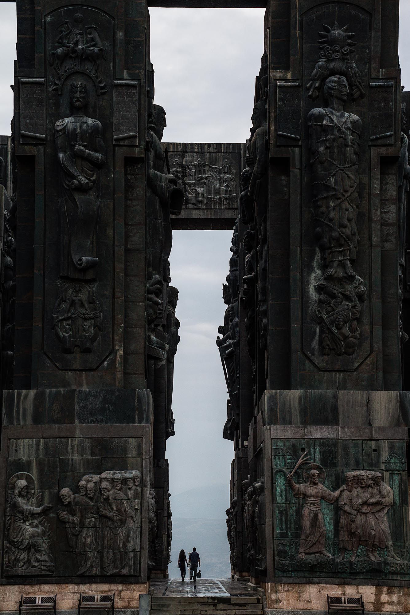 Silhouettes of people walking past ornate stone carvings at the Volkerschlachtdenkmal monument in Leipzig, Germany.