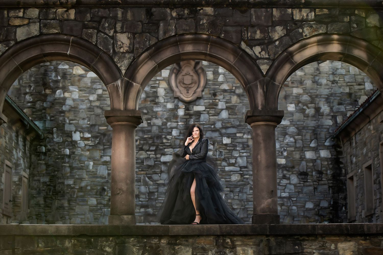 Lady in a large black couture dress in front of a stone building with arches at a cemetery in Atlanta Georgia while doing a photo session