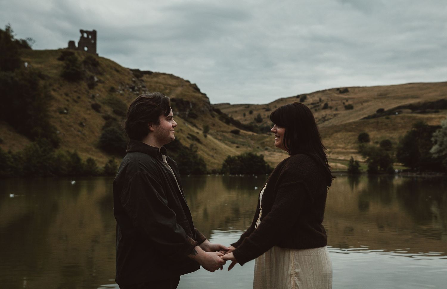 Romantic couple engagement photos taken by a lake with dramatic cloudy skies in the background.