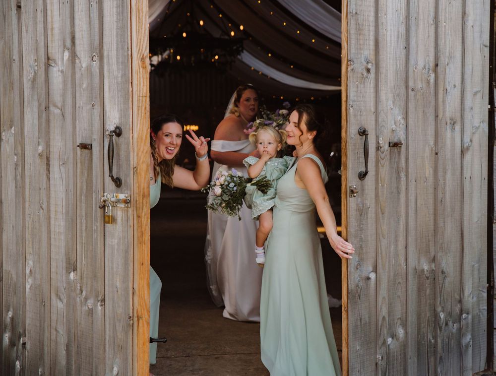 Outdoor wedding at Moor Farm Barn, Weymouth. Bridesmaids in sage green bridesmaids dresses wave. From a candid Dorset Wedding Photographer