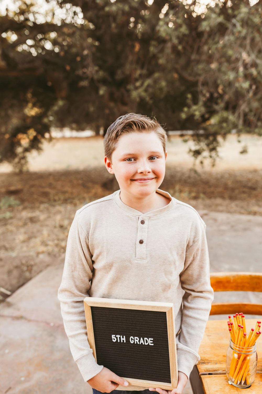 A student in a beige sweater poses with a letter board outdoors during a photo session.
