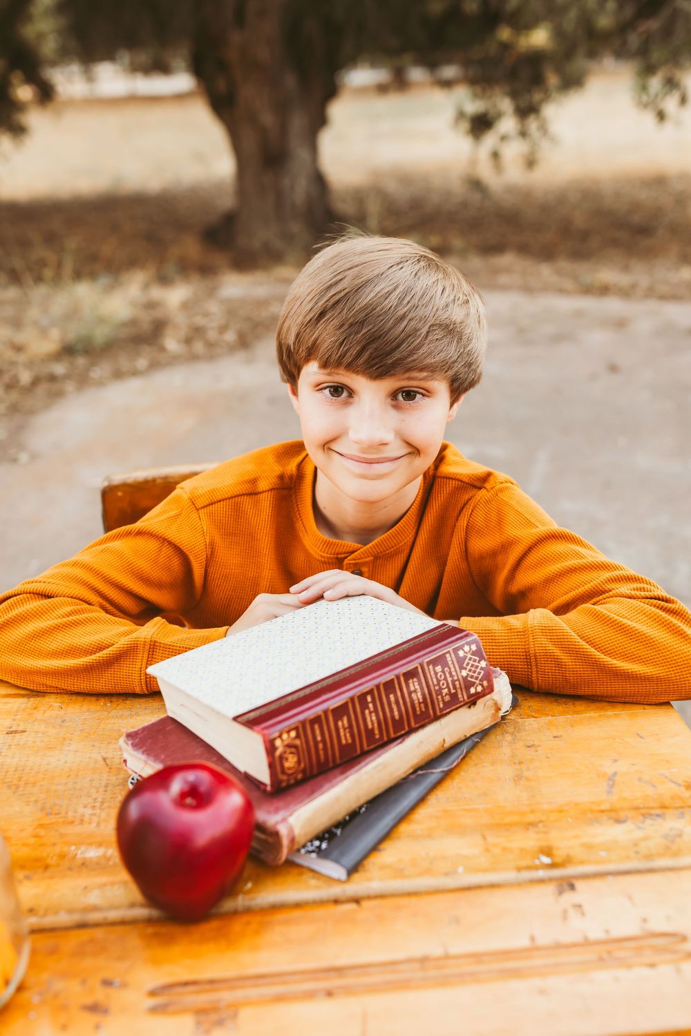 A student lies on an orange table with books and an apple in an outdoor setting.