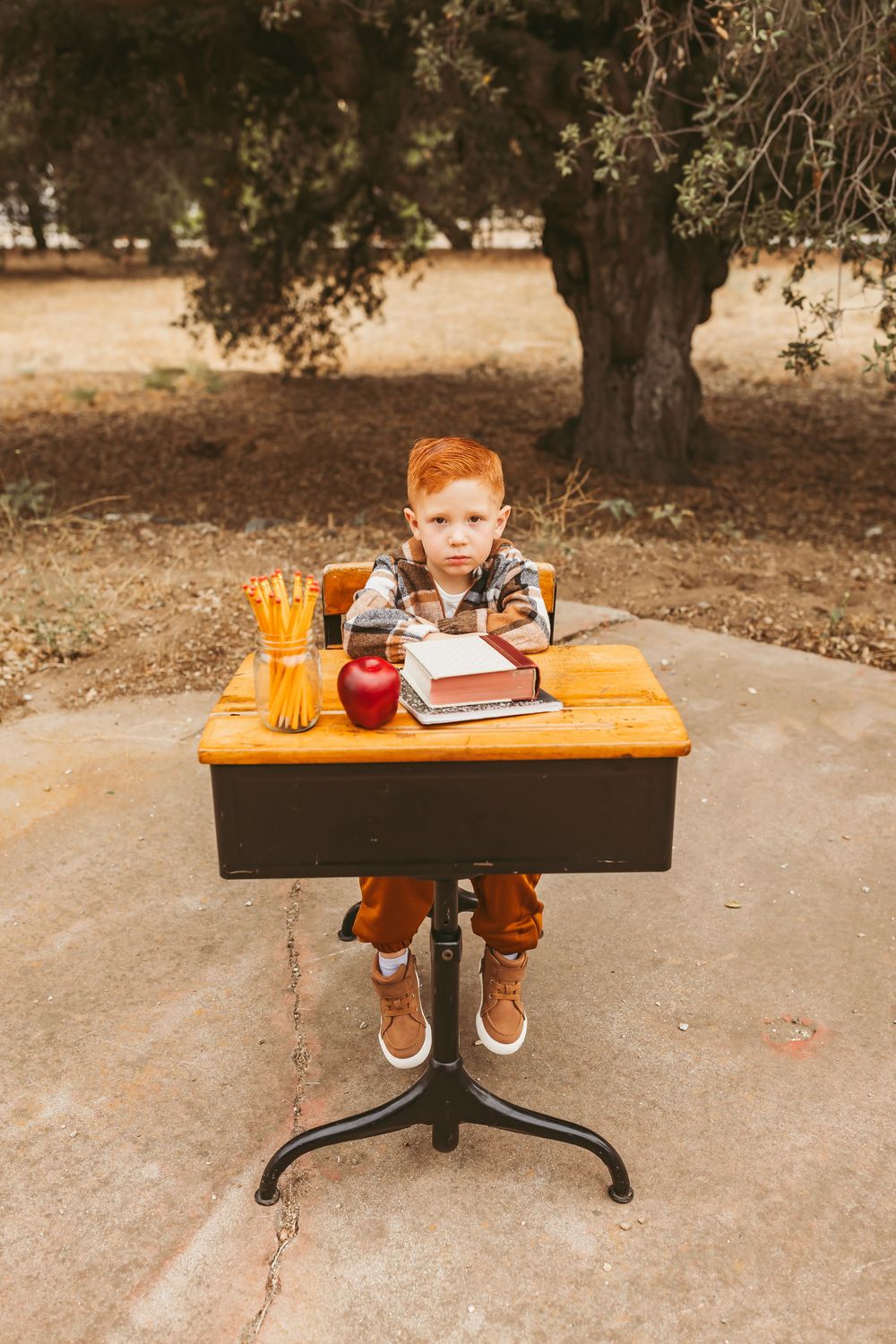 A dark wooden table outdoors displays school supplies, an apple, and a pumpkin in a fall-themed composition.