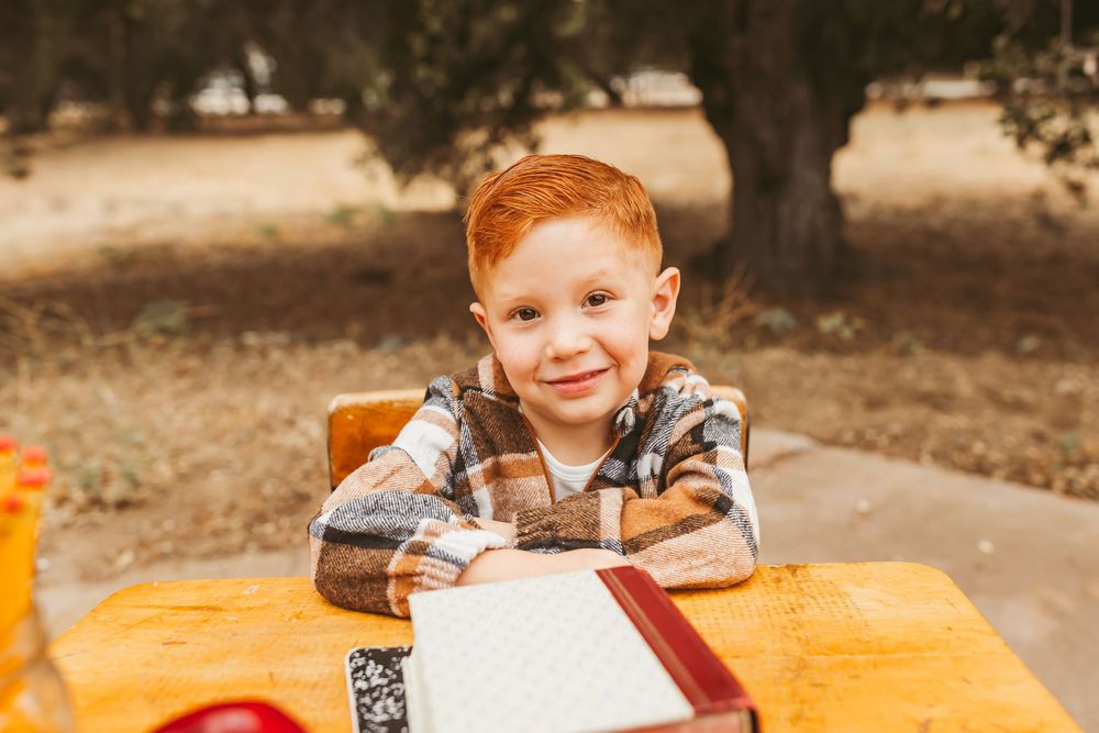 A young child sits at a wooden picnic table outside during autumn while working on an activity.