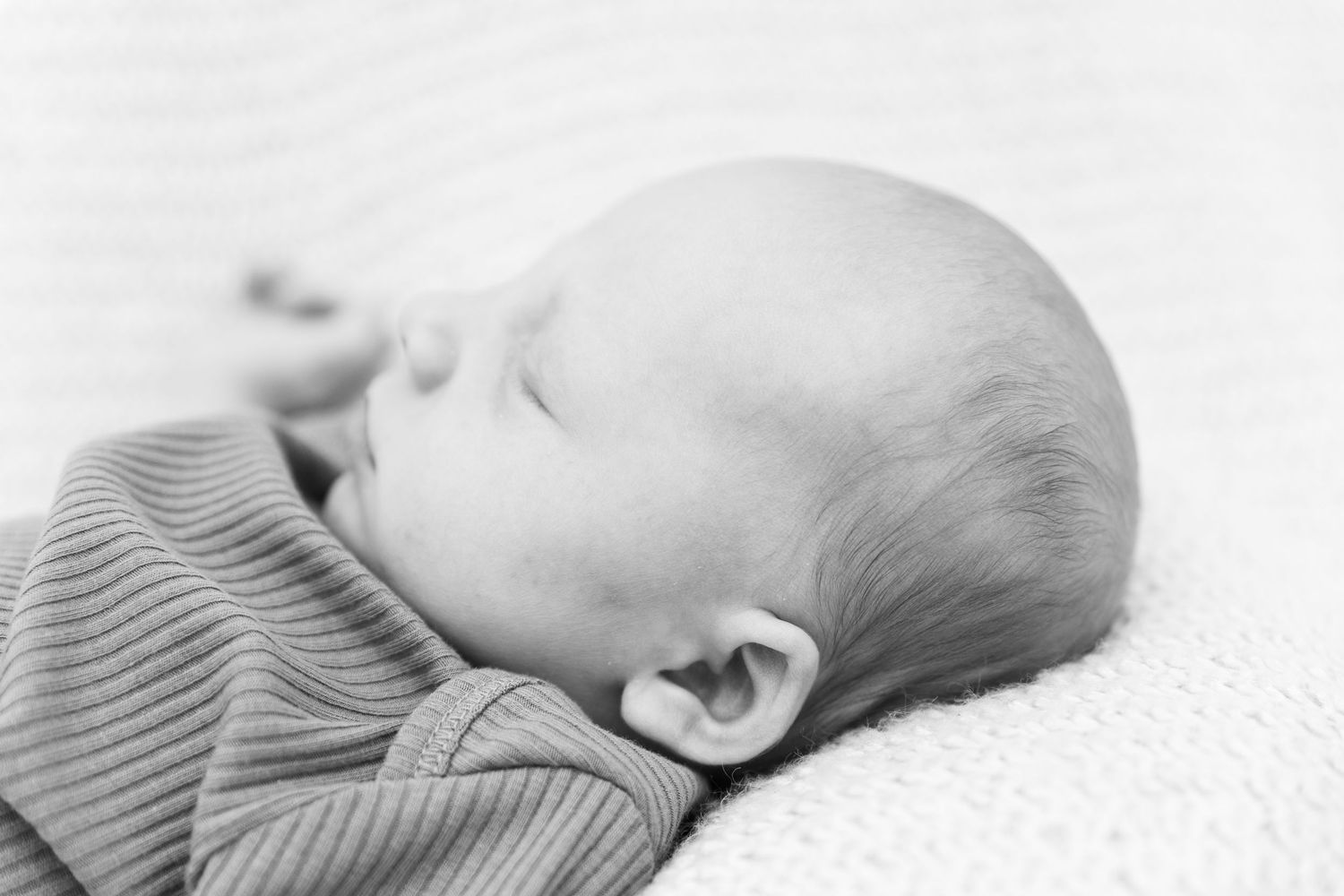 A small baby wearing a blue knit hat rests peacefully in a brown woven basket.
