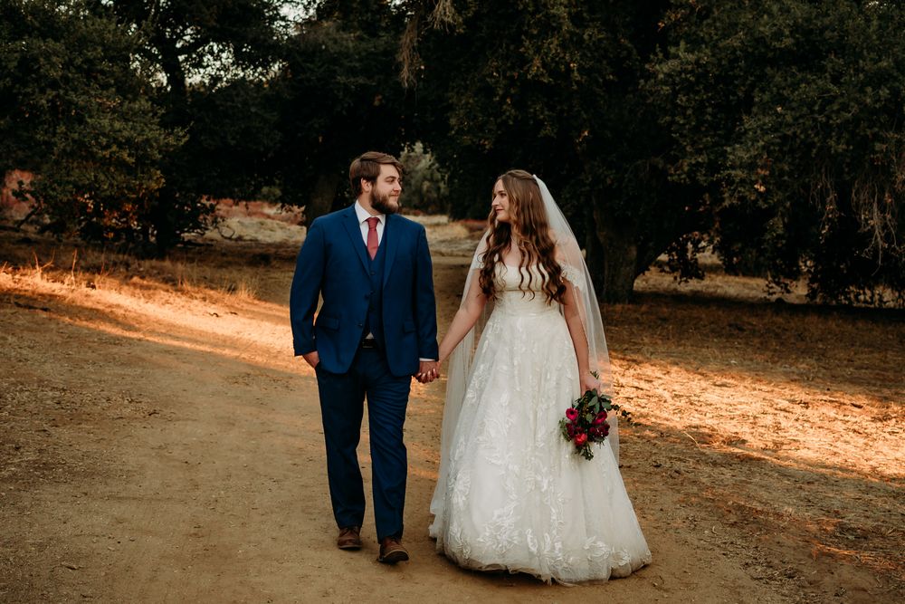 Couple walking along a path looking at each other with trees behind them