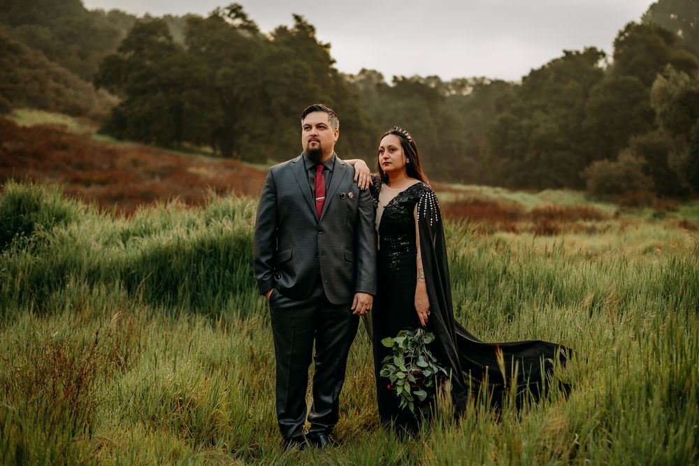 Couple standing in a field with trees behind them and are looking off into the distance.