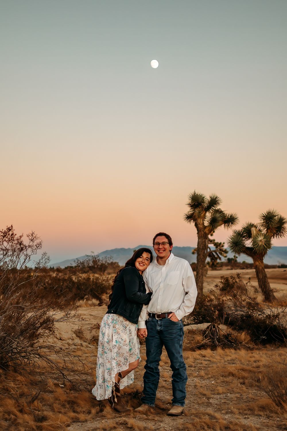 Couple, standing, looking at the camera with mountain and Joshua trees in the background.