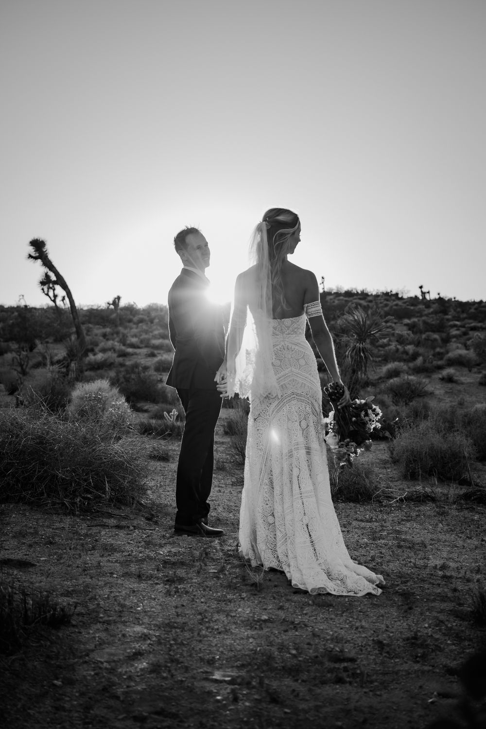 Silhouetted couple poses in a desert landscape at sunset with Joshua trees in the background.