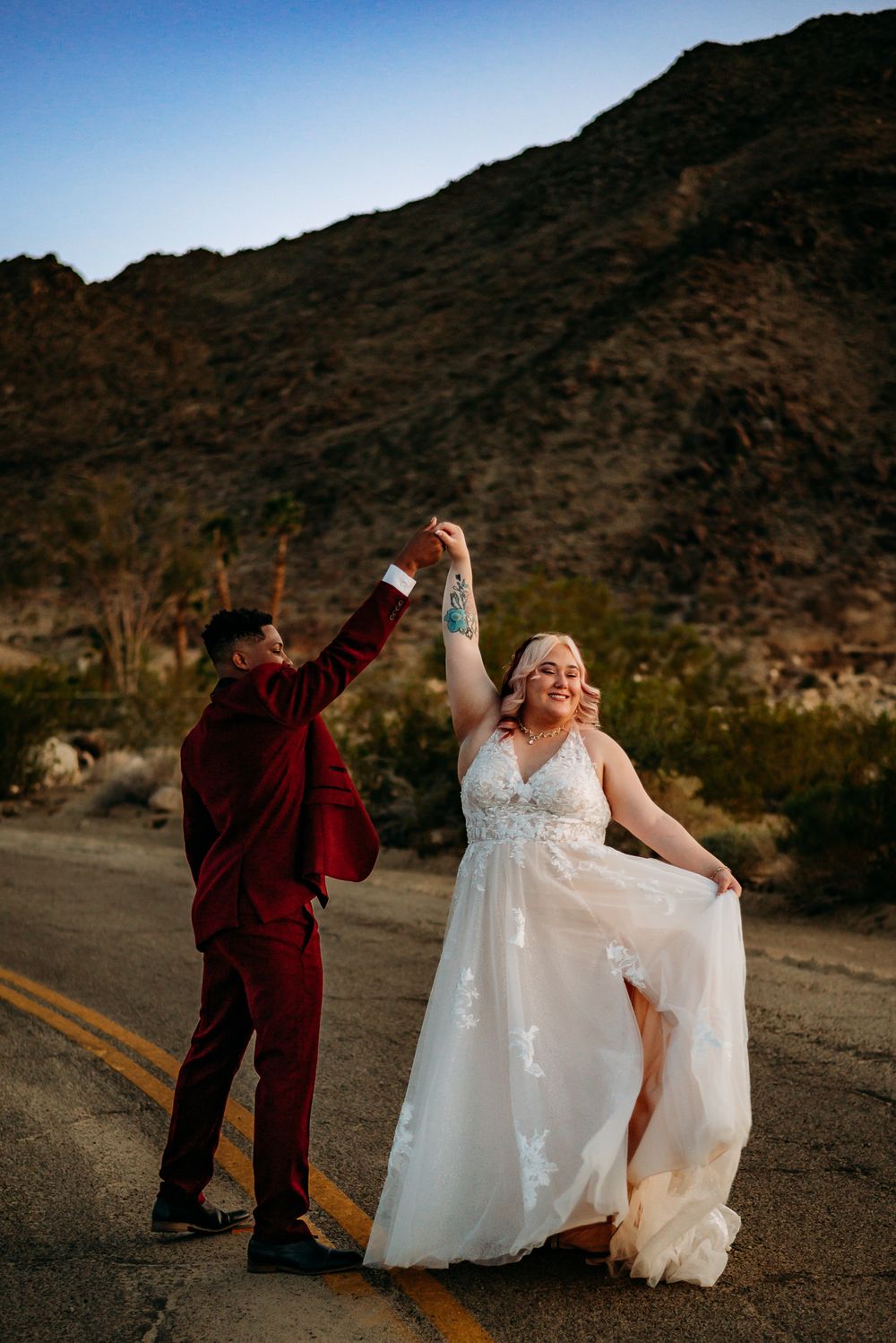 A couple dances on a desert road with mountains in the background during their wedding.