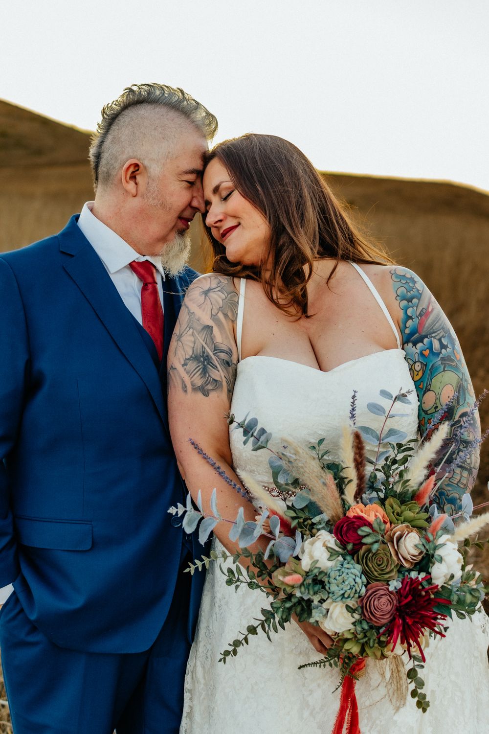 Romantic couple embracing while holding a vibrant floral bouquet against a natural backdrop.