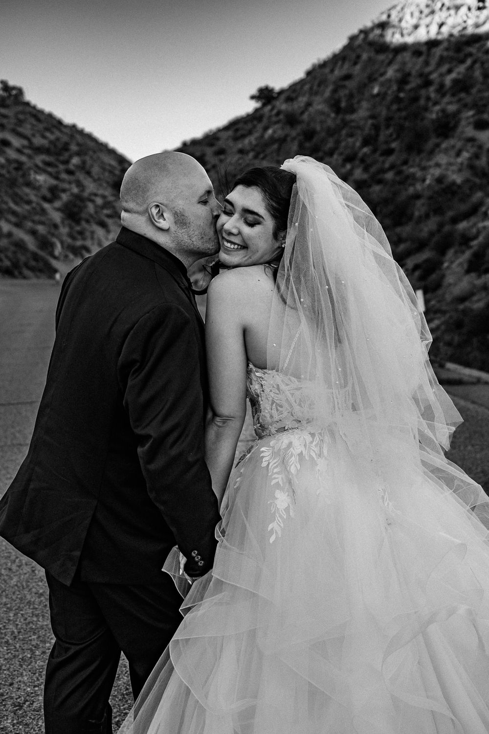 Black and white portrait of couple sharing intimate moment in dramatic mountain landscape.