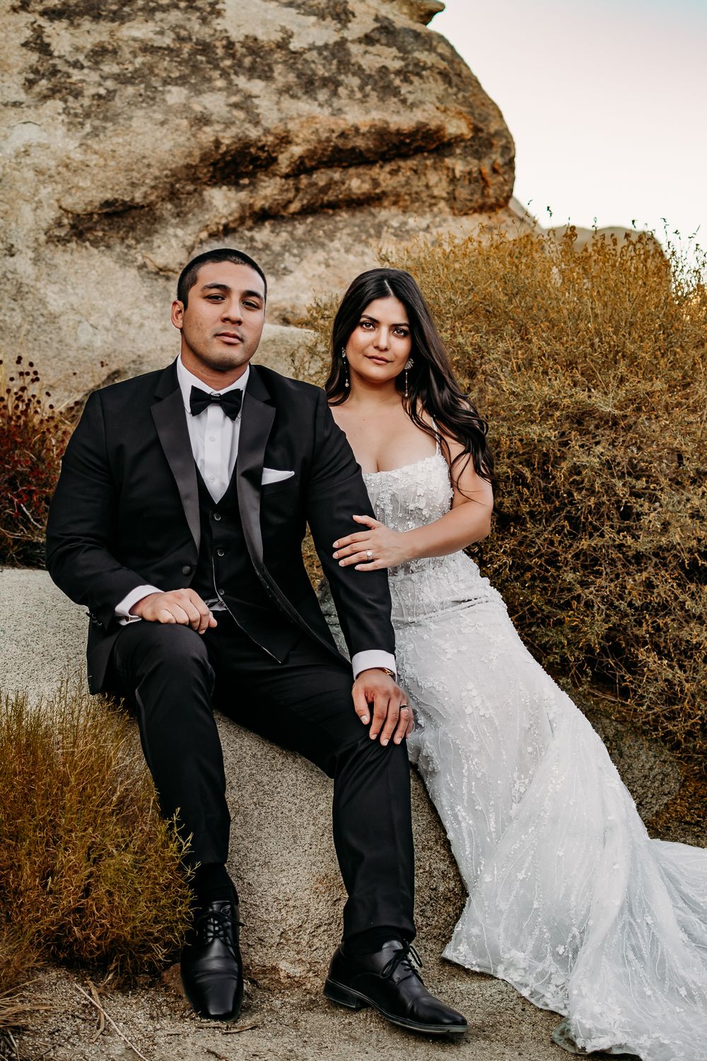 A formal wedding portrait of a couple seated against a large boulder.