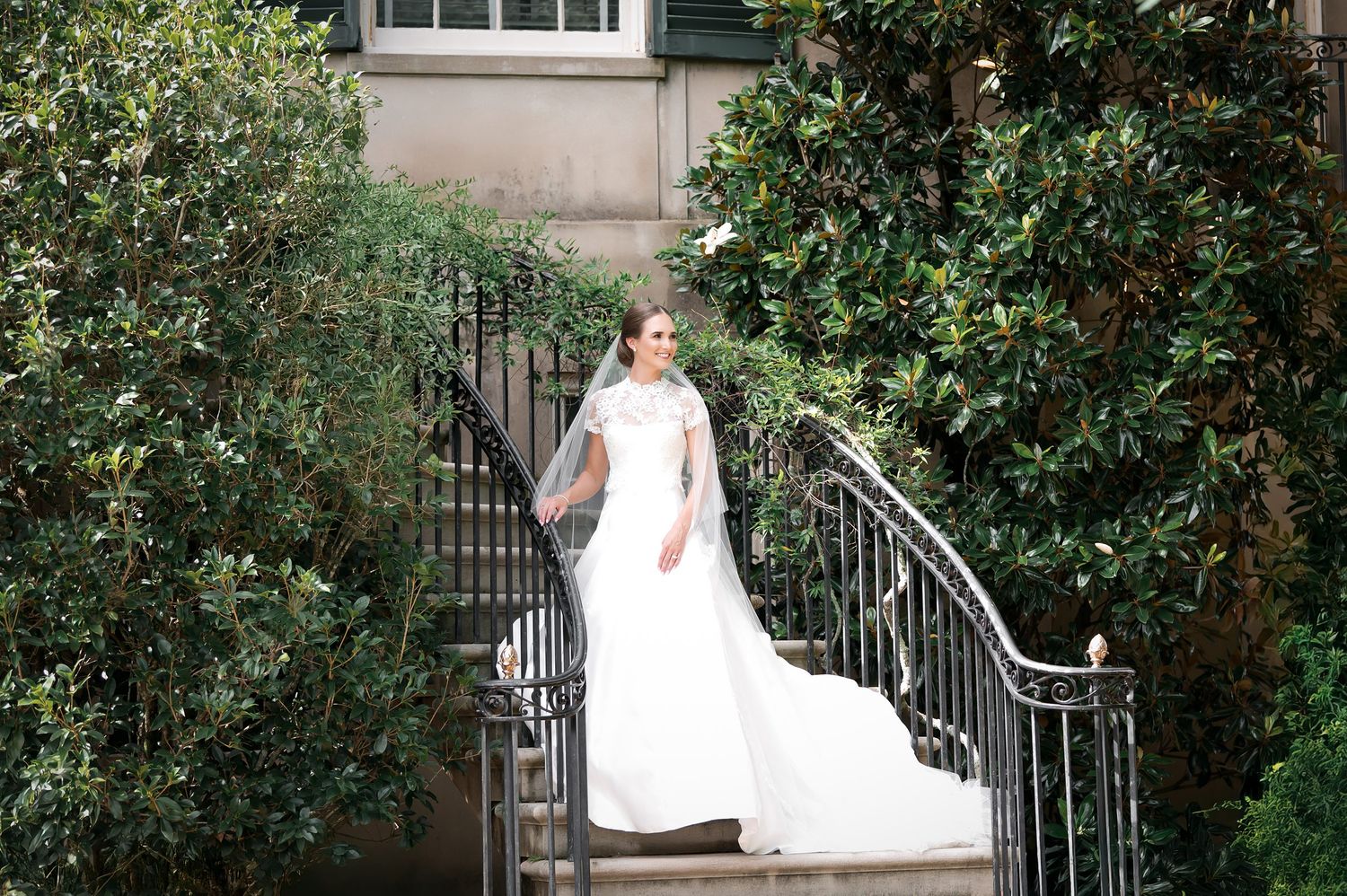 A classic bridal portrait on stone steps surrounded by green foliage and architectural details.