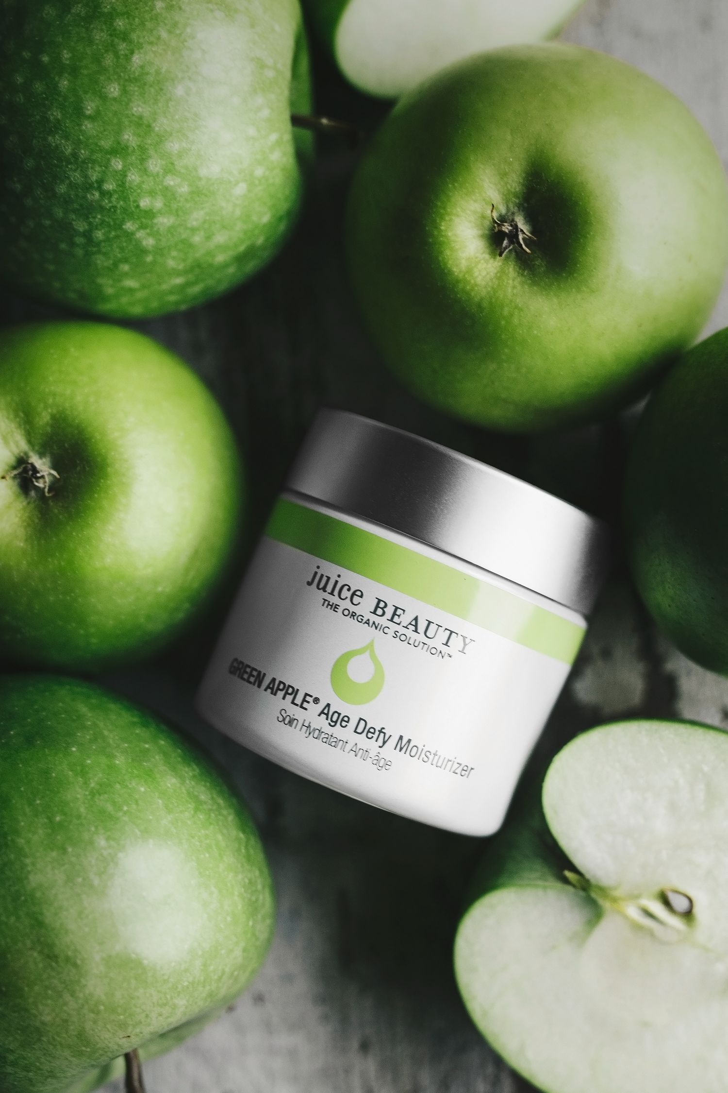 Produktfoto av Juice Beautys Green Apple Age Defy Moisturizer som ligger bland gröna äpplen, ljuset kommer från sidan