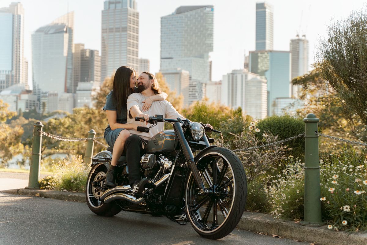 Harley motorcycle parked in an urban setting with city skyscrapers and autumn foliage in the background during a proposal photoshoot in Syd