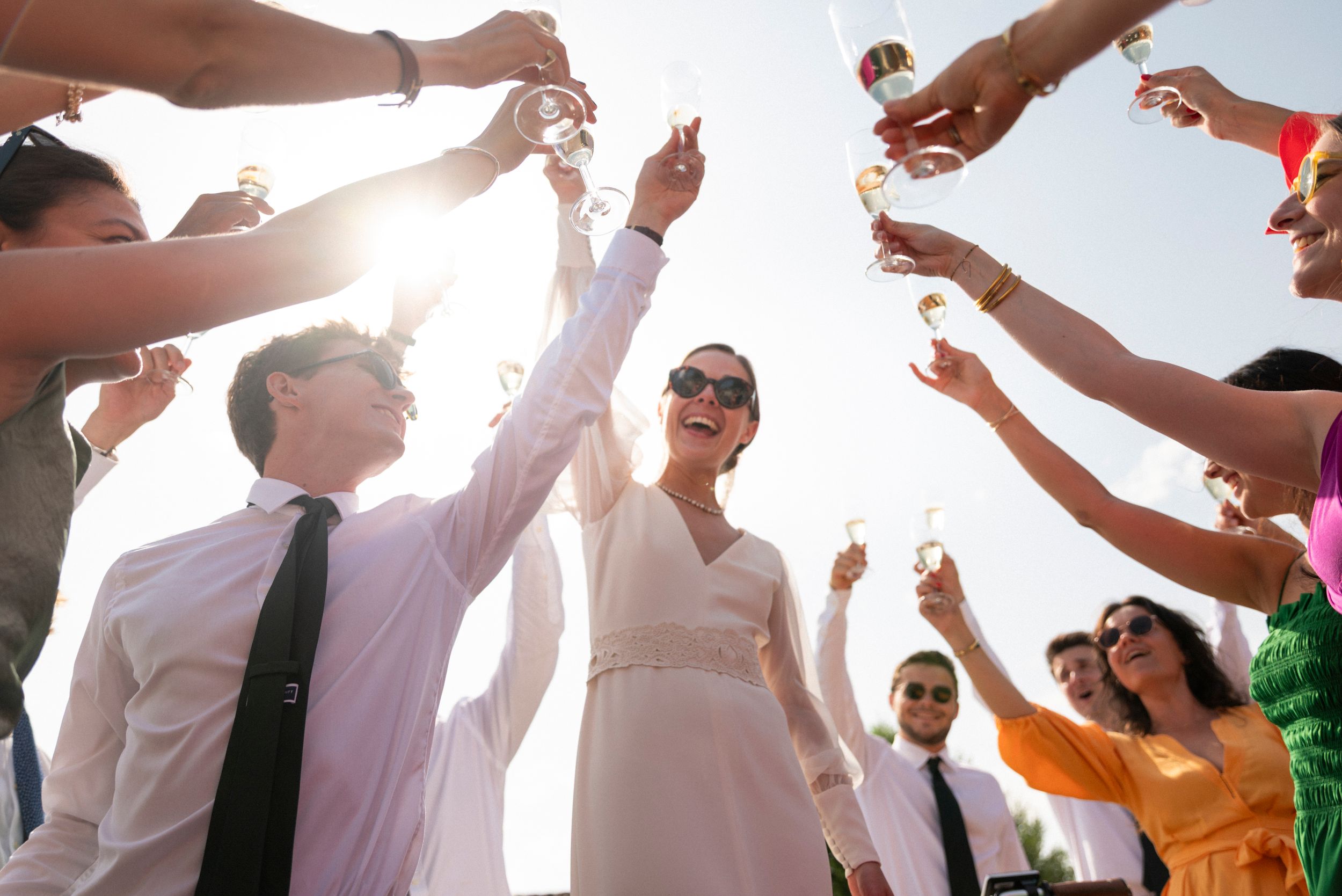 Group of wedding guests dancing and raising hands together during outdoor celebration at sunset.