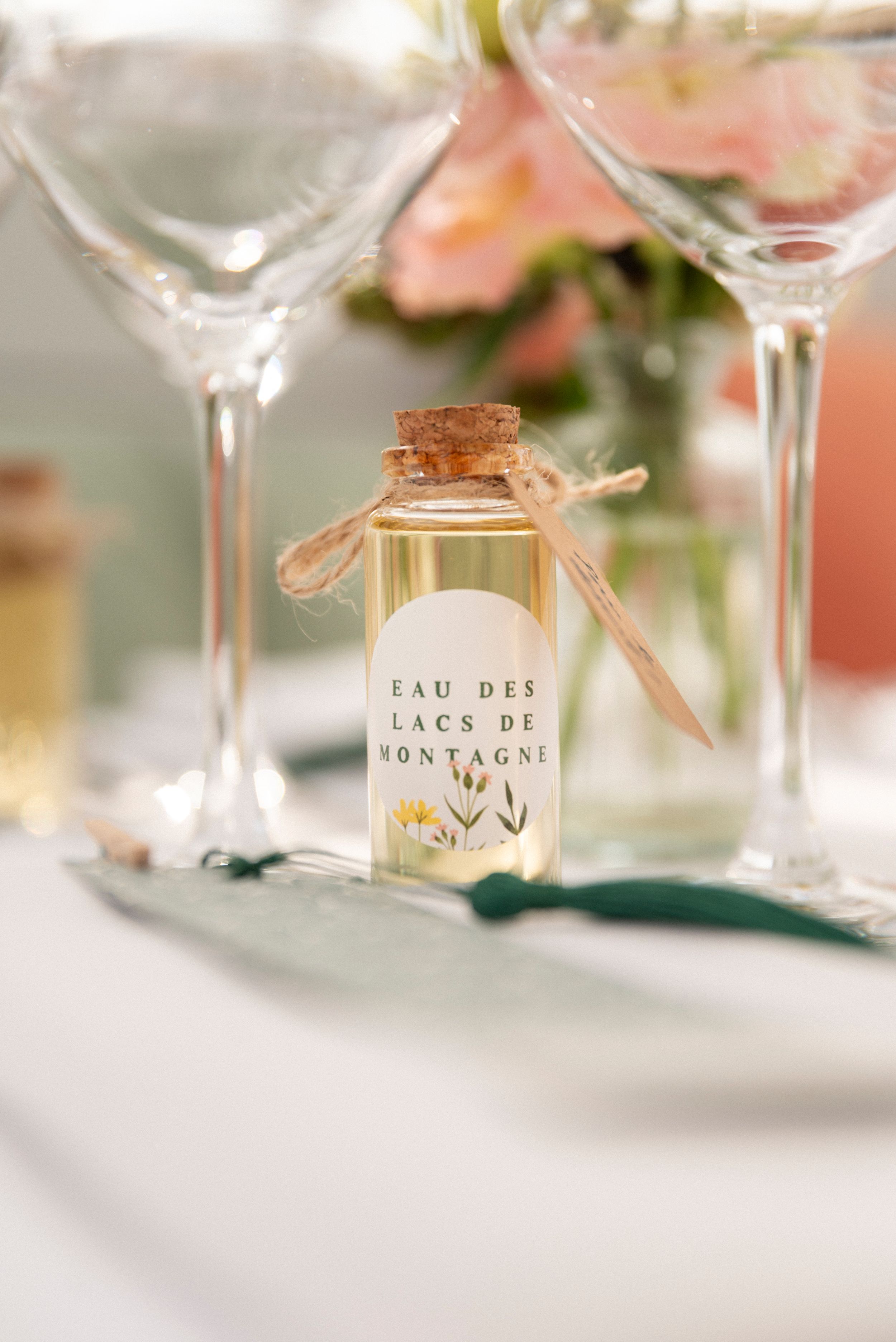 Elegant wine glasses and perfume bottles arranged in soft focus with delicate pink floral accents in the background.