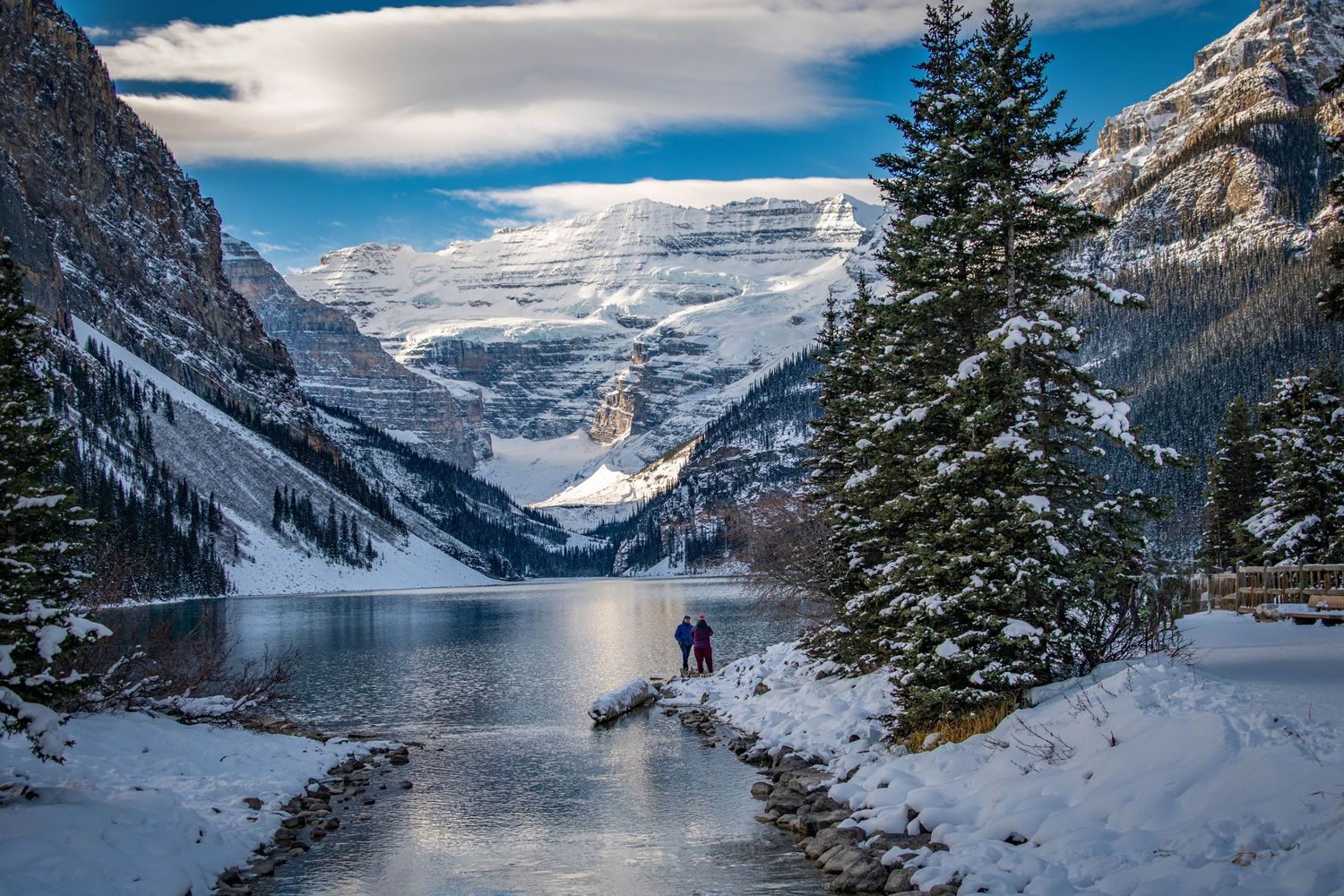 Panoramic winter view of Lake Louise in Banff National Park with snow-covered mountains and evergreen trees.