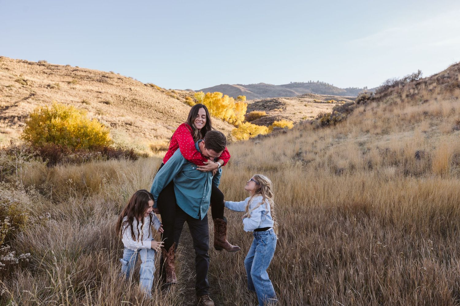 Family playing and walking together in a golden autumn field with mountains in the background.