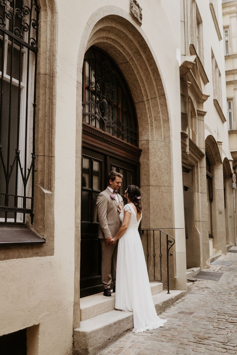 A couple stands in an elegant stone archway entrance with wrought iron details and a wooden door in a historic setting.