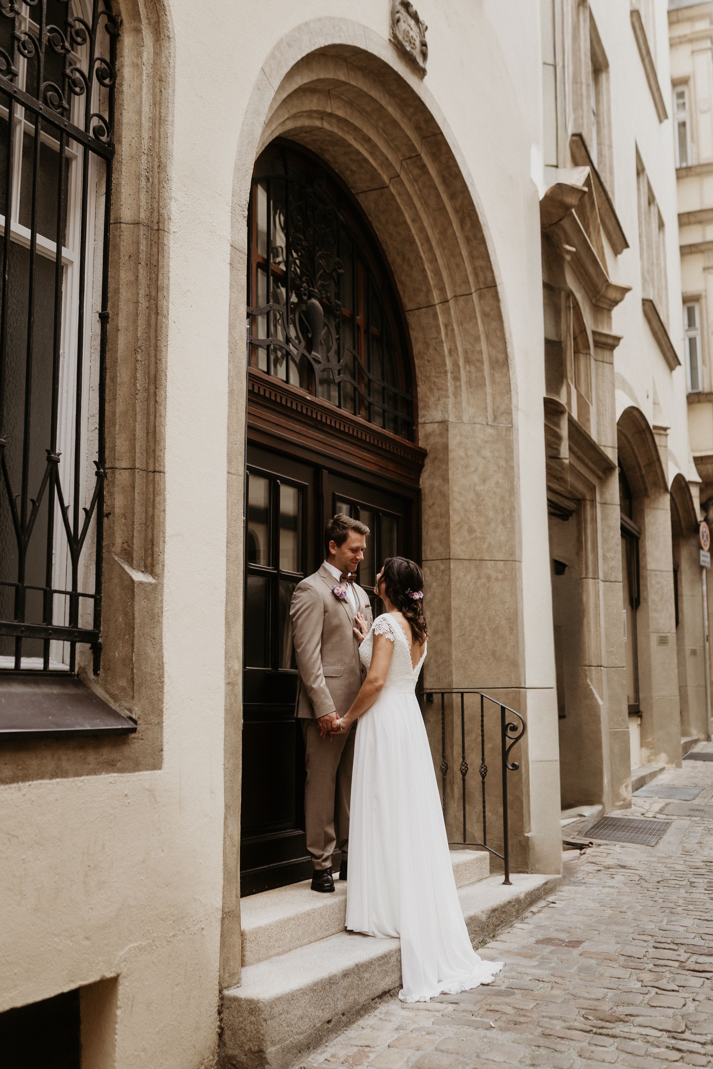 A couple stands in an elegant stone archway entrance with wrought iron details and a wooden door in a historic setting.