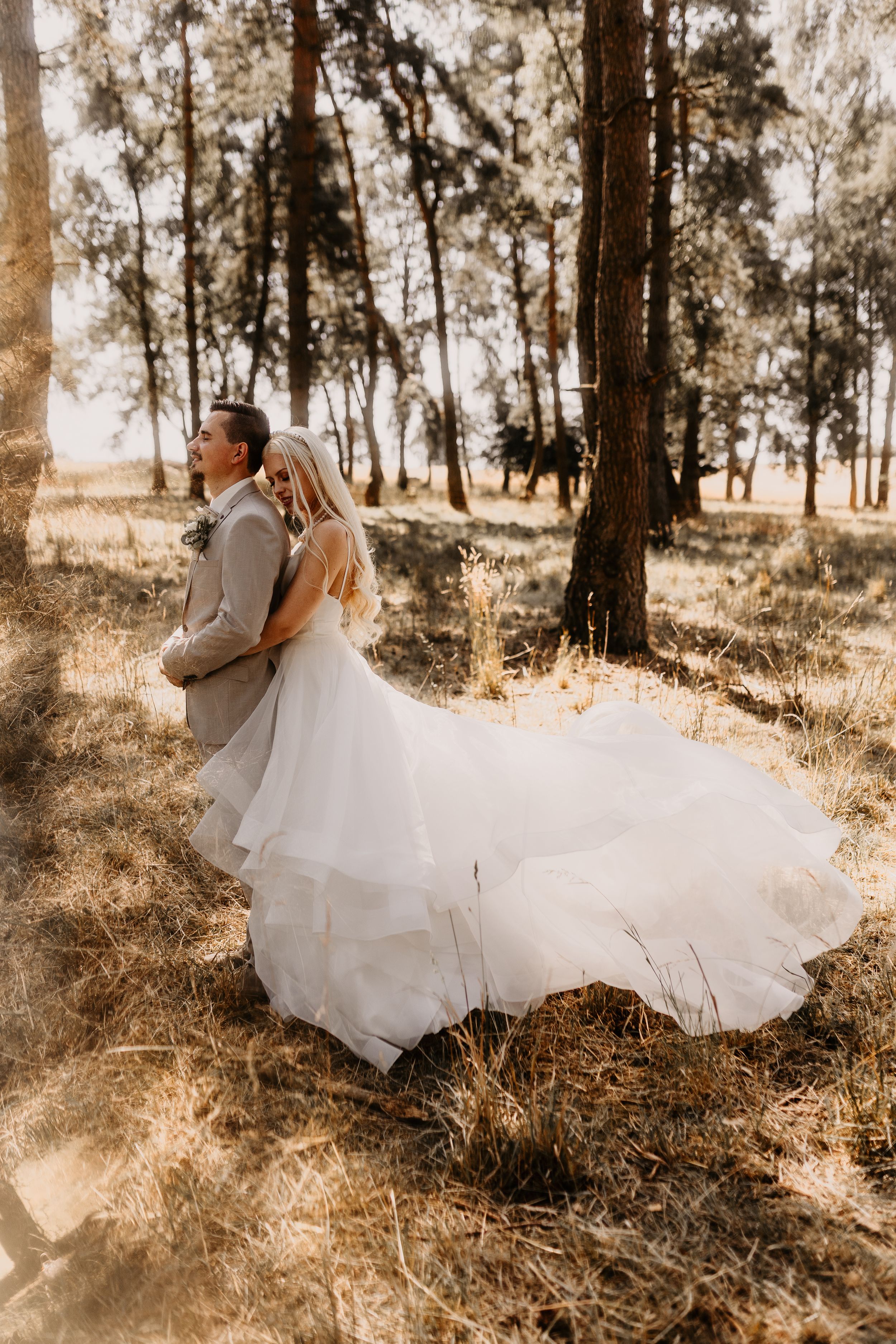 A romantic forest wedding scene with a flowing white dress trailing through sunlit trees and tall grass.
