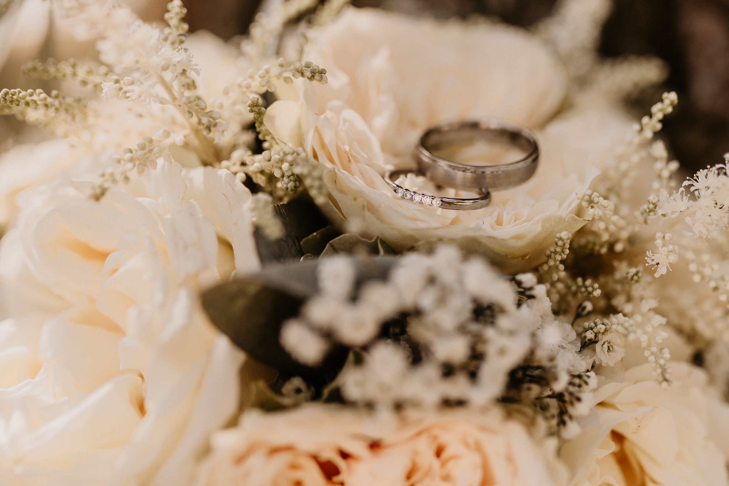 Delicate white and blush floral wedding bouquet with baby's breath and roses arranged on a light surface.