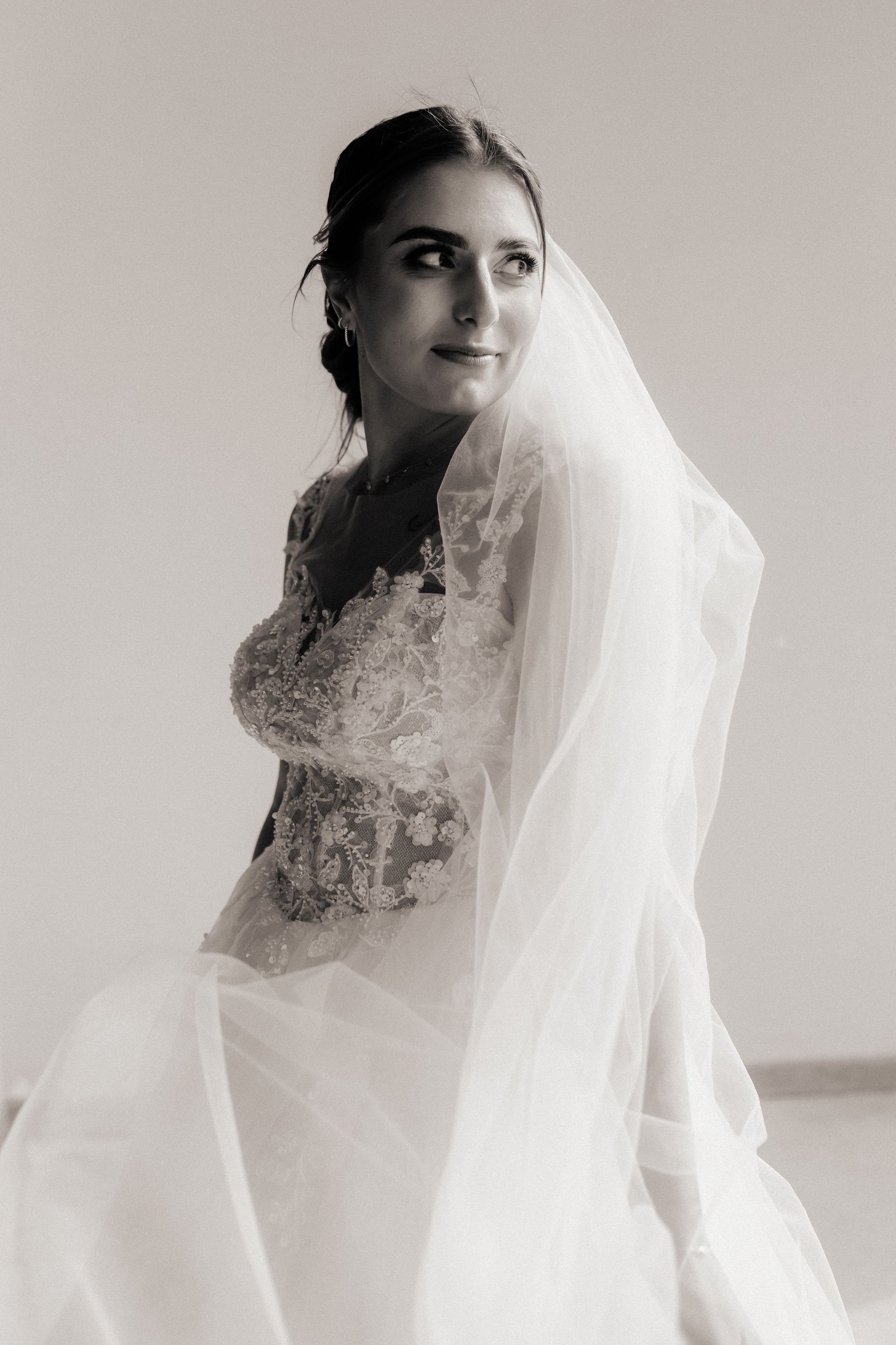 Black and white portrait of a bride wearing a delicate lace wedding dress and flowing veil.