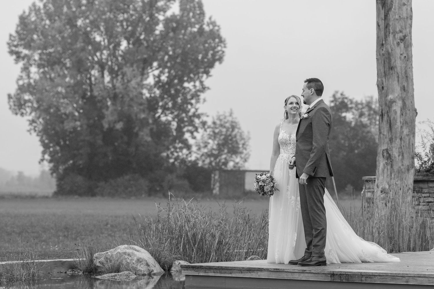 A couple in wedding attire stands together during golden hour in a scenic outdoor setting.