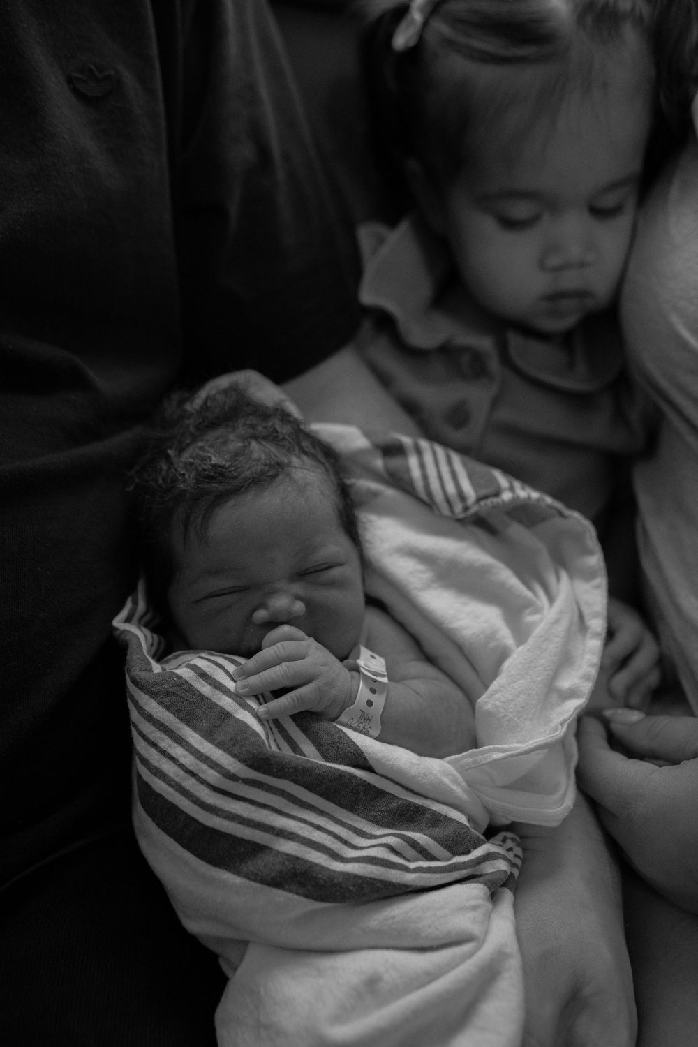 Newborn wrapped in striped blanket resting in hospital bassinet.