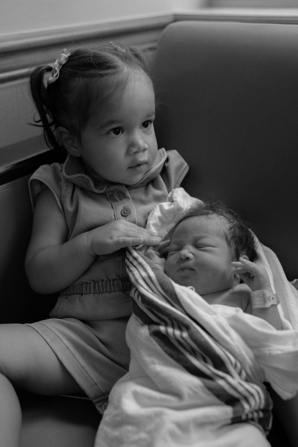 Black and white series showing tender sibling moment of young child gently holding and caring for sleeping baby.