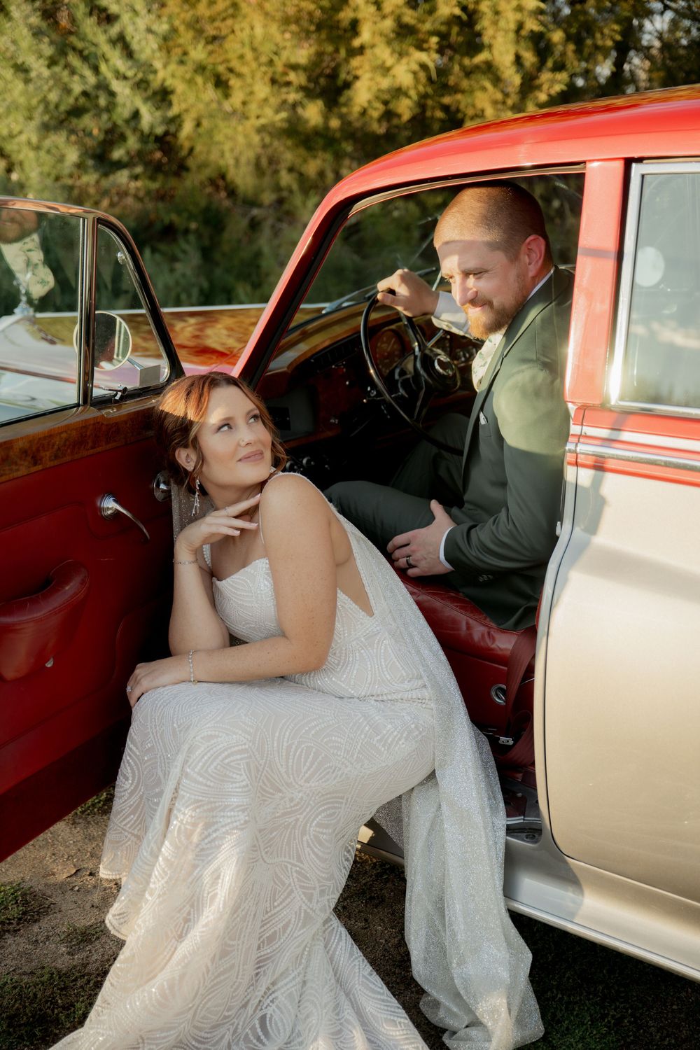 A vintage red and white classic car serves as a romantic backdrop for a couple in wedding attire.
