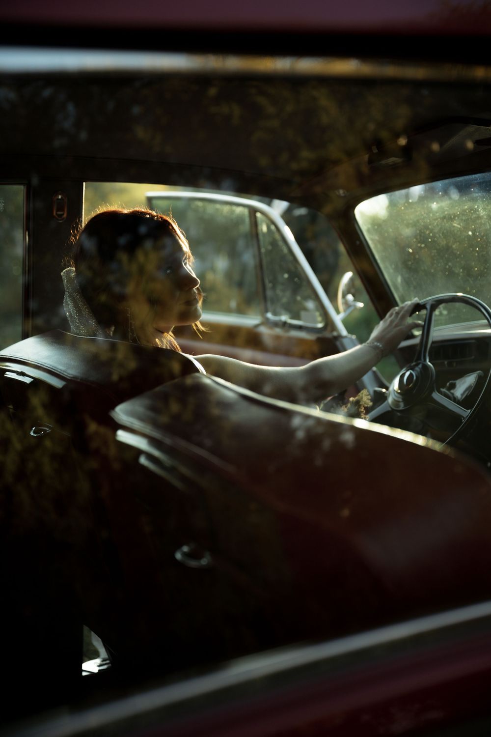 A person sits in the driver's seat of a car at night with dim lighting creating a moody atmosphere.