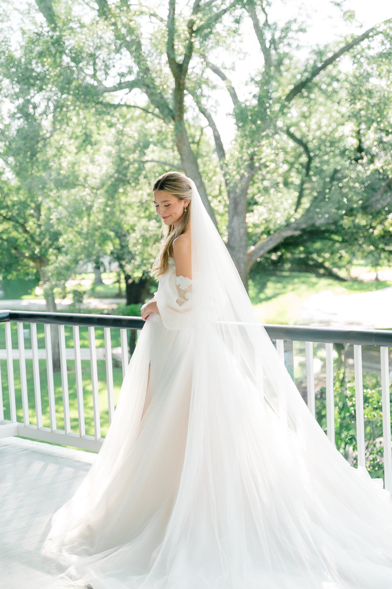A flowing white wedding gown and long veil captured in an ethereal outdoor setting with lush greenery and sunlight.