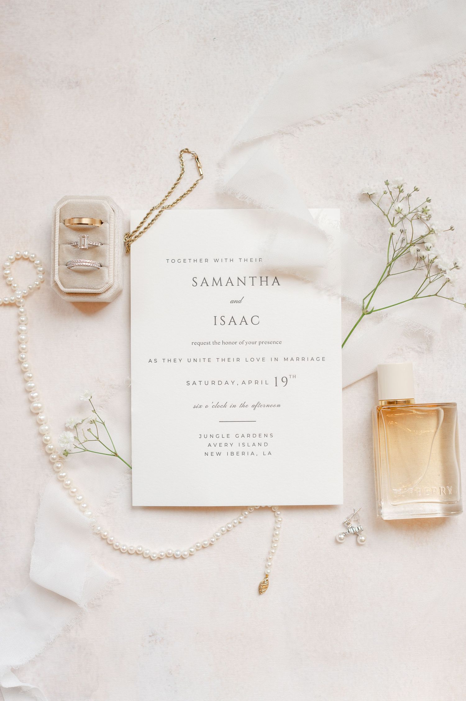 Elegant wedding invitation with white stationery, perfume bottles, delicate baby's breath flowers and pearl necklace on light background.