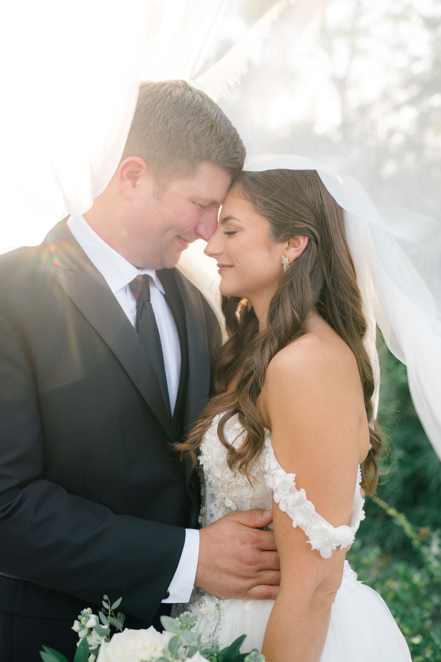 A romantic wedding couple shares an intimate moment in a sun-drenched garden setting.
