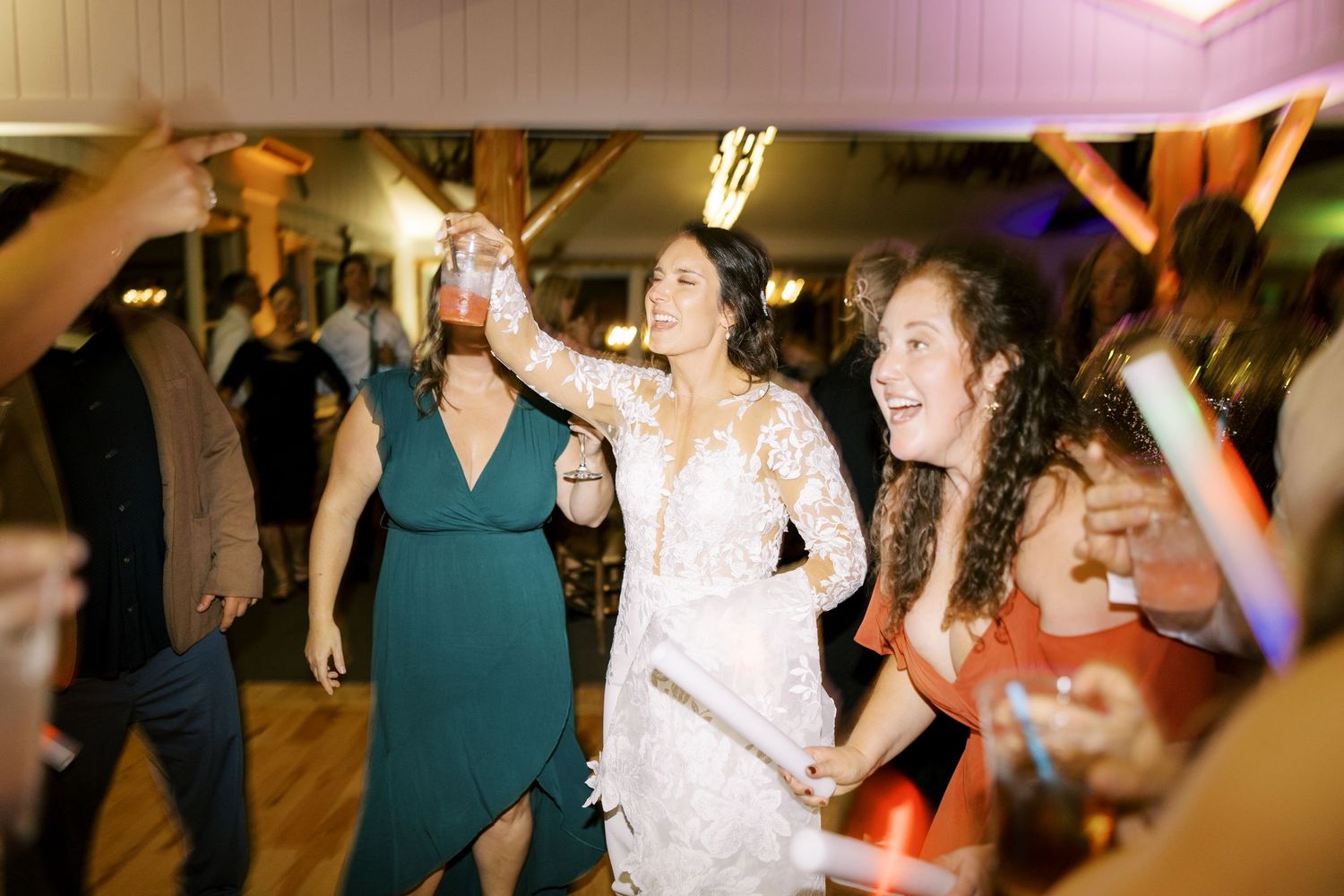 Joyful wedding guests dancing together on a wooden dance floor during an evening reception celebration.