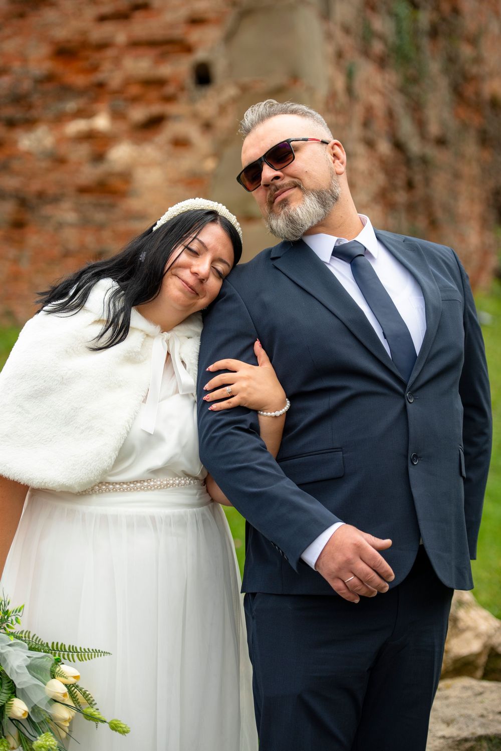 A wedding couple poses playfully in a series of photos showing them leaning on each other against a brick wall background.