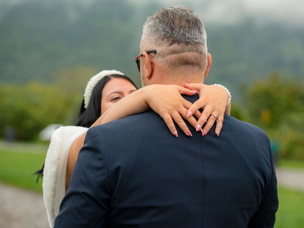 Wedding couple embracing in front of lush green landscape during outdoor photoshoot.