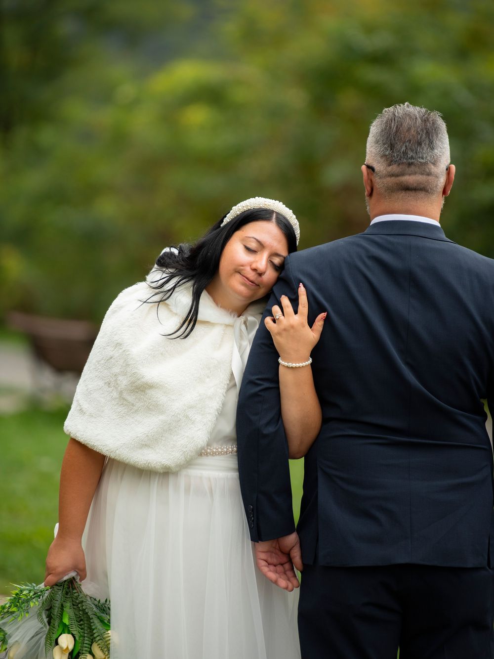 Bride in white dress and groom in black suit share intimate moment during outdoor wedding photos.
