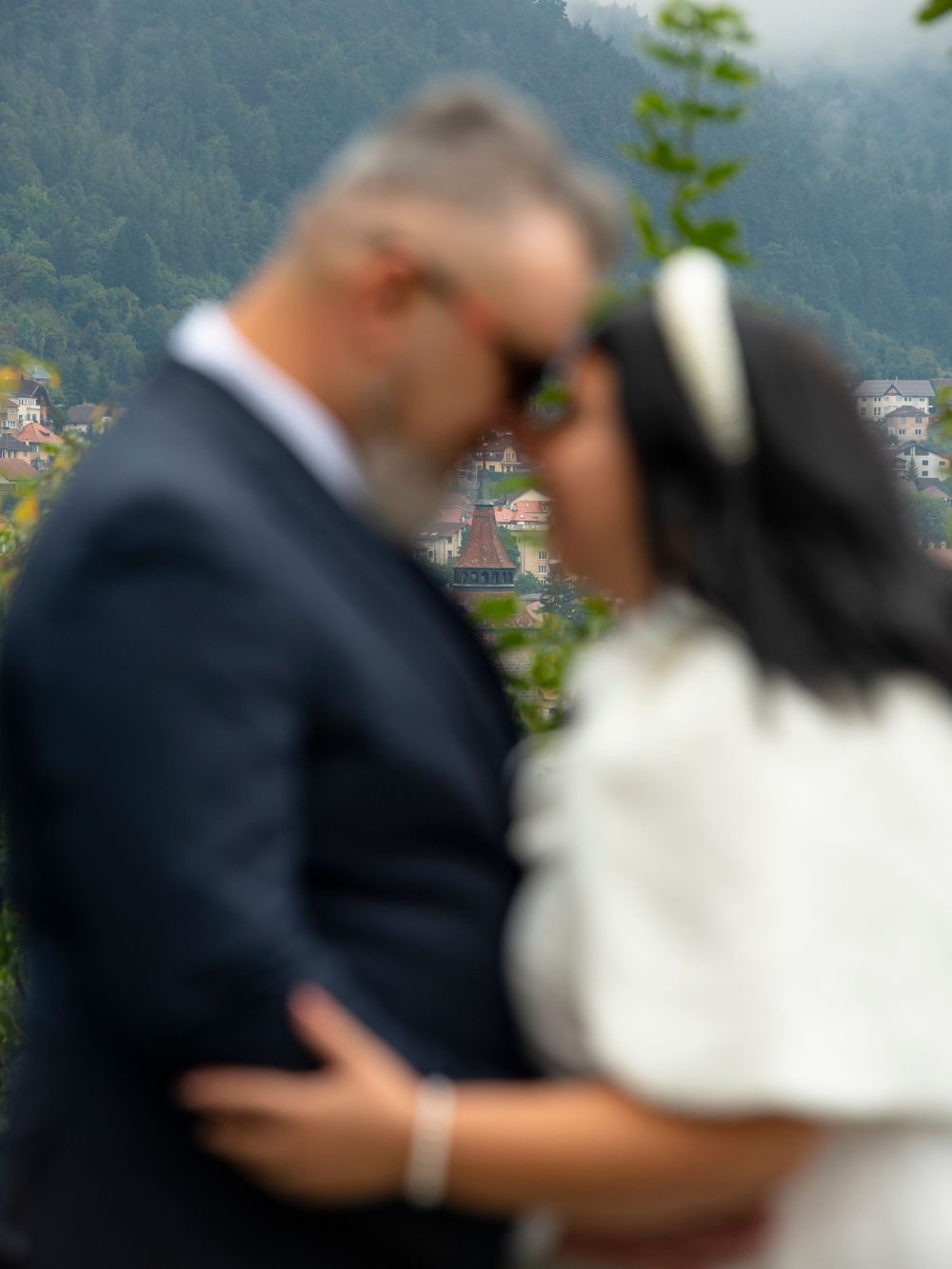 A romantic wedding couple embraces in a tender kiss against a blurred mountain landscape background.