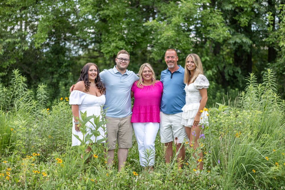 A family smiles together in a wildflower field during a photo session at Centennial Park in Springfield, IL