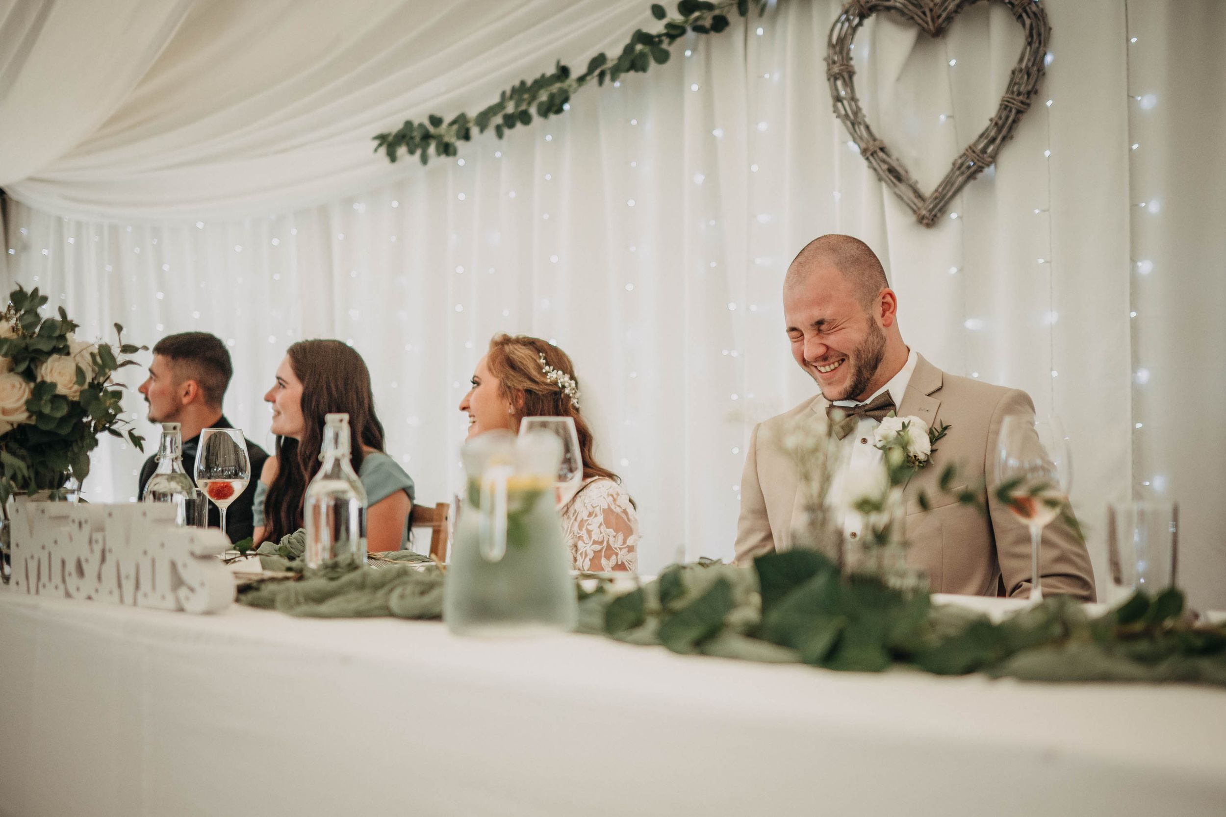 Wedding reception in an elegant white marquee tent with heart decorations and greenery.