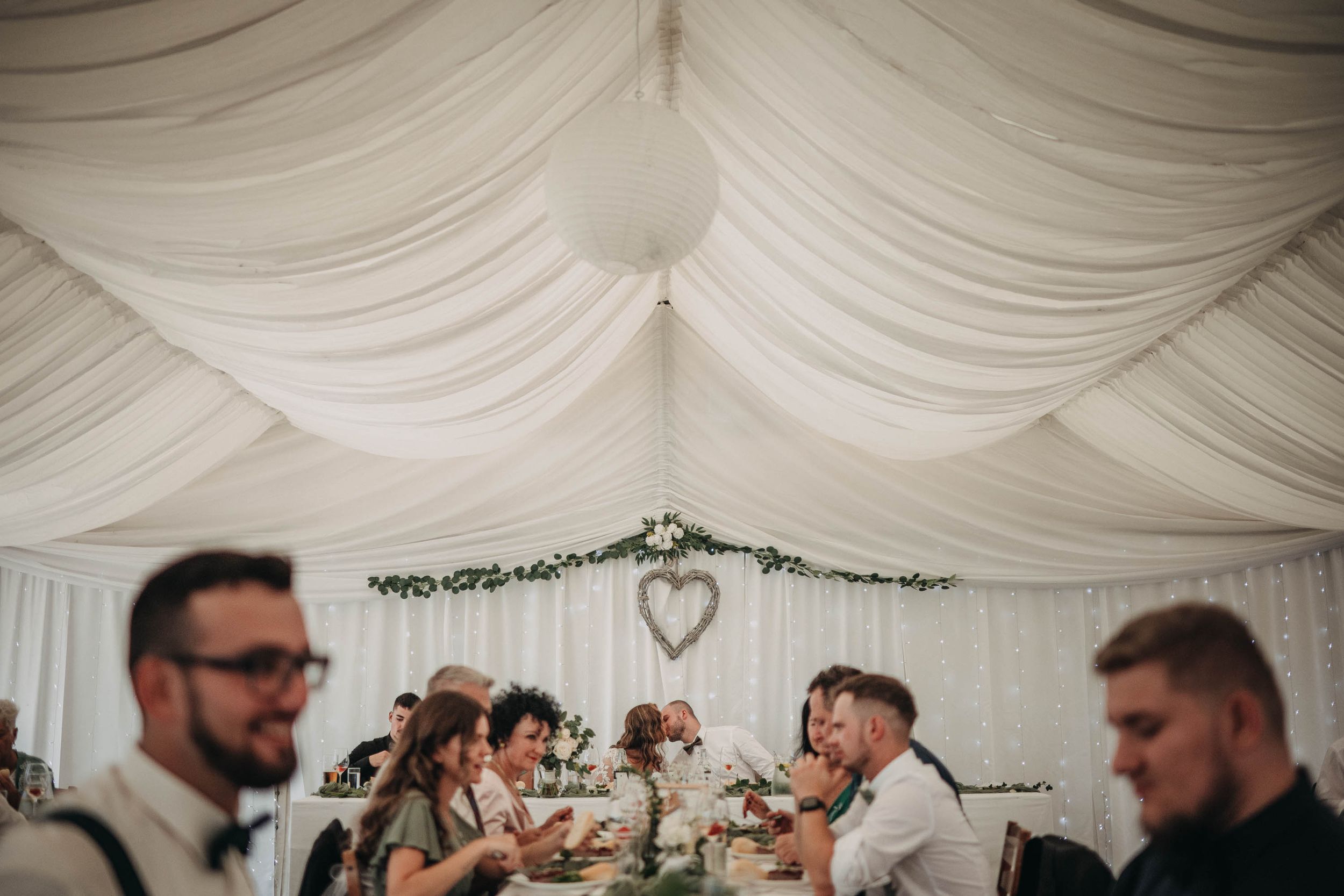 Interior of a decorated wedding marquee with draped white fabric ceiling and string lights.