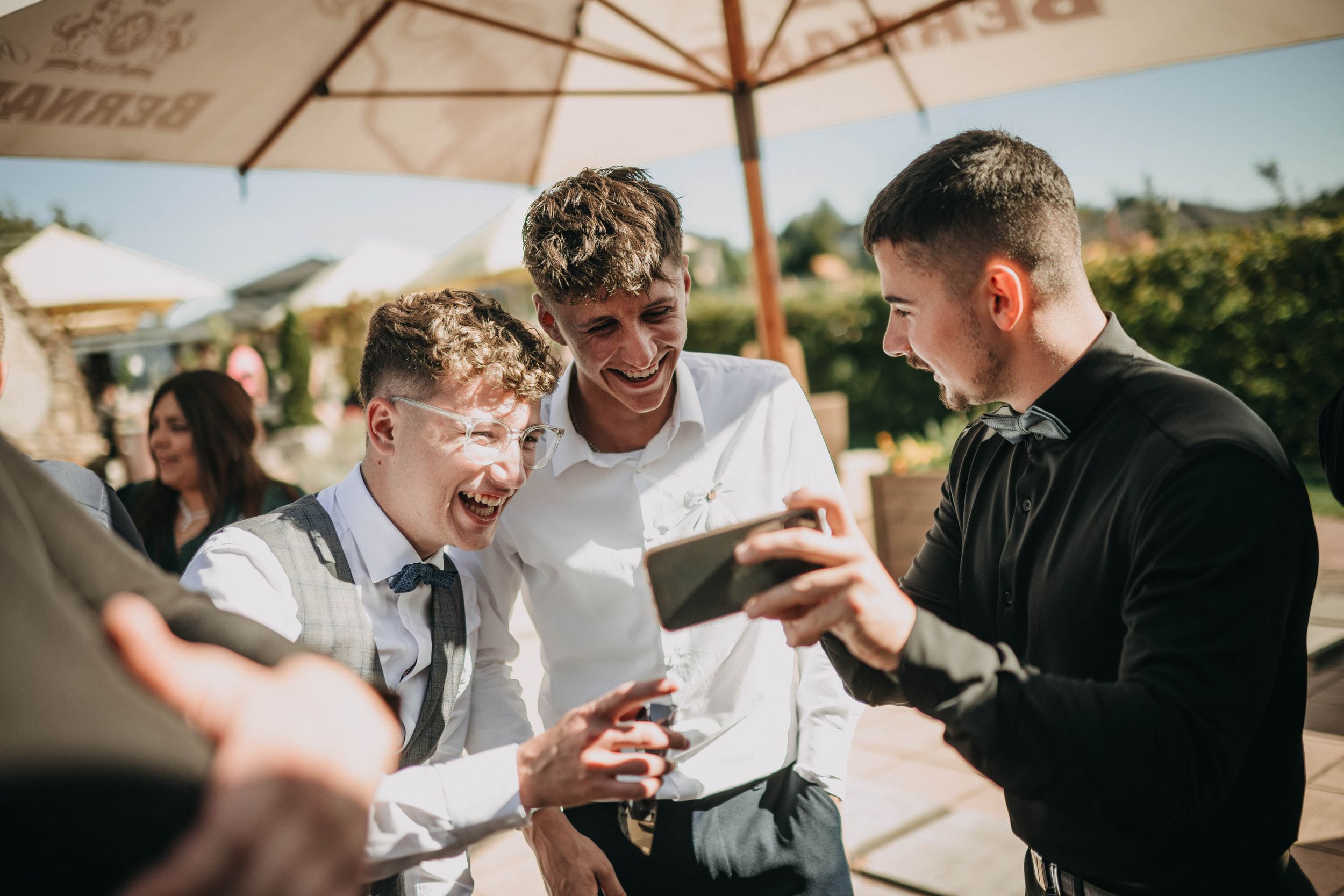 Wedding guests enjoying drinks and conversation under outdoor umbrellas.