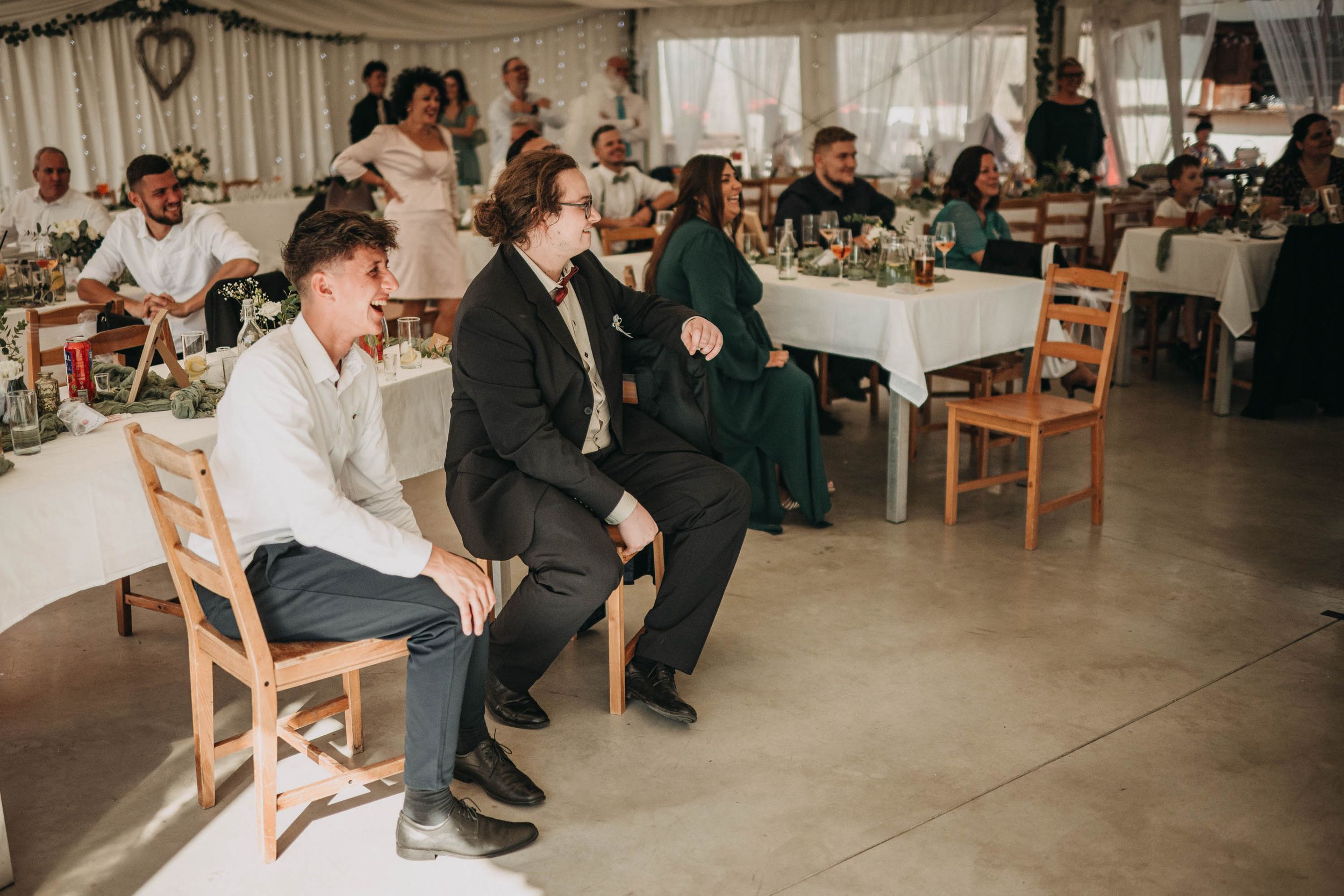 Wedding reception venue with guests seated at wooden tables inside a white marquee.