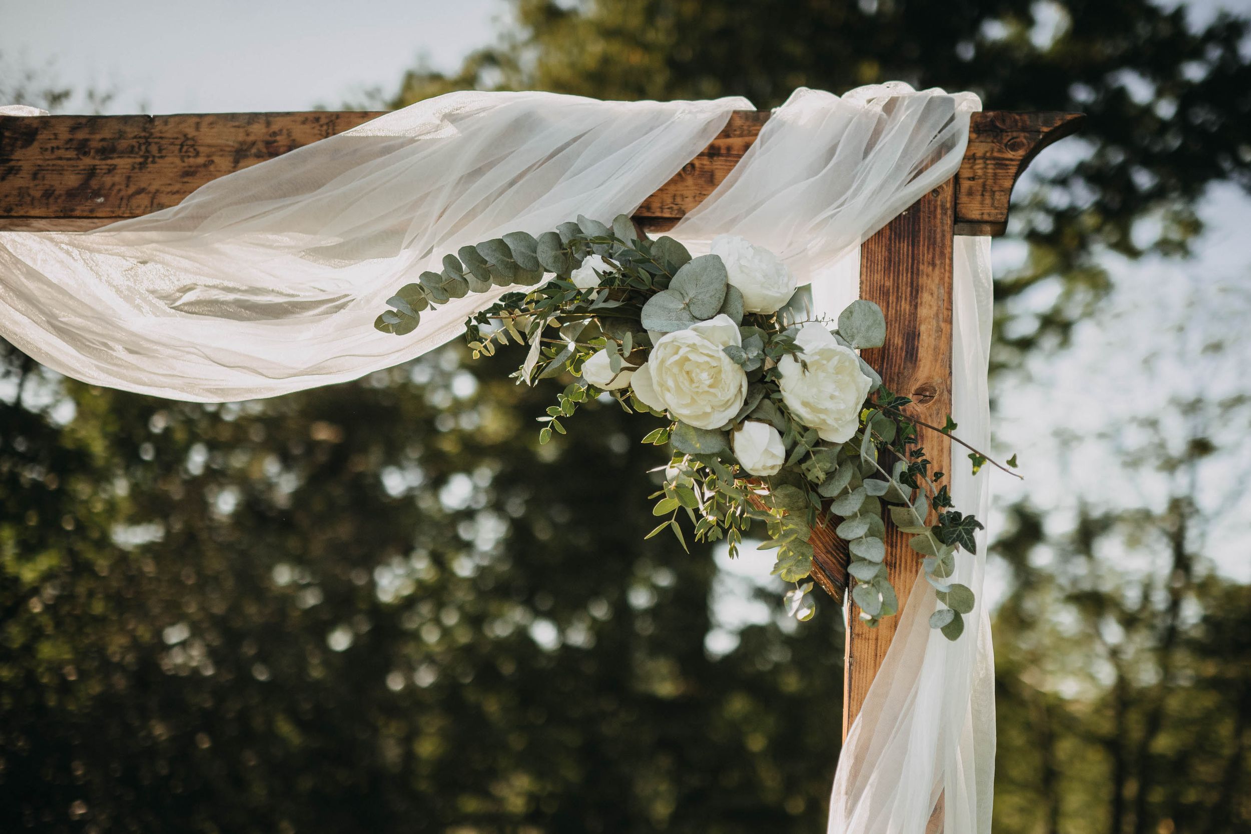 Outdoor wedding arch decorated with white fabric and eucalyptus against a natural backdrop.